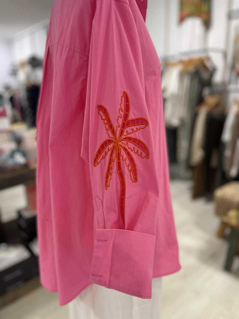Pink shirt with red palm tree design hanging in a store