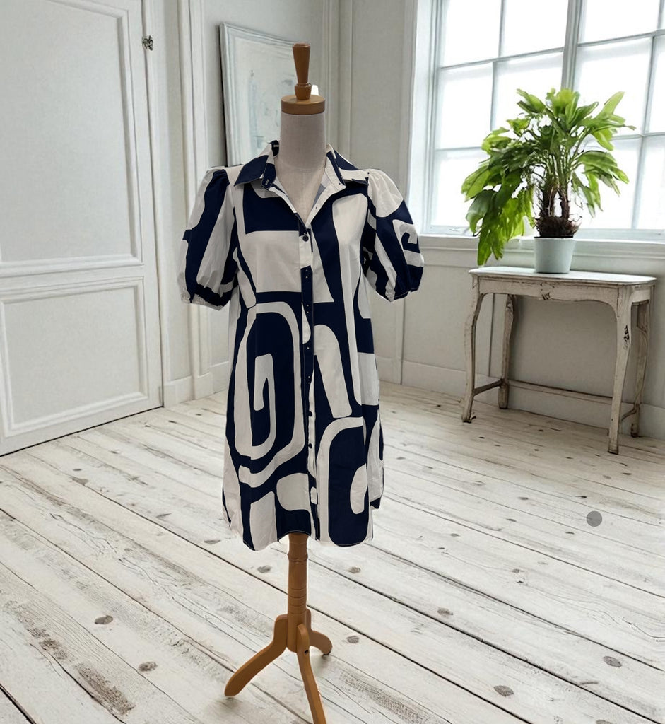 Blue and white patterned dress on a mannequin in a room with a wooden floor and a plant.