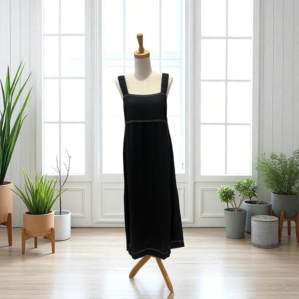 Black dress on a mannequin in a room with large windows and potted plants.