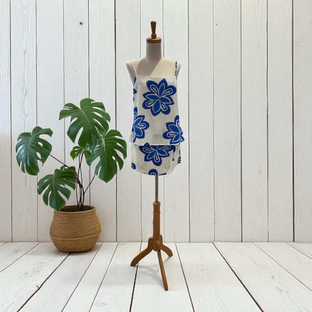 Mannequin with a floral skort and top on a wooden stand next to a potted plant against a white wooden wall.