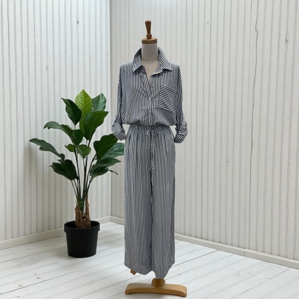 Mannequin wearing a striped shirt and wide-leg pants with a plant in the background.