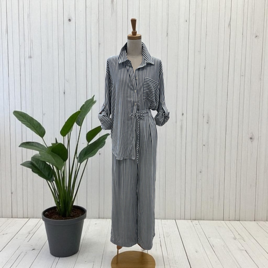 Mannequin wearing a striped outfit with a plant on a wooden floor and white wall background