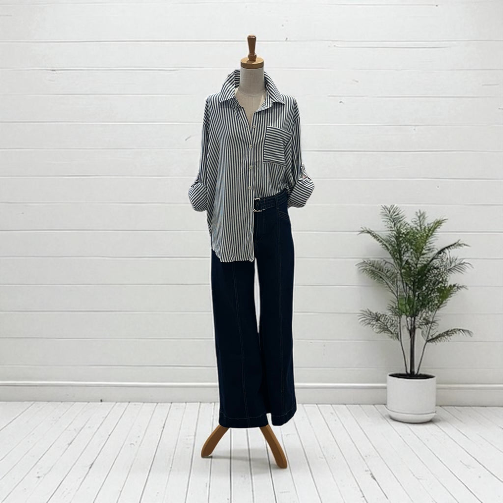 Mannequin wearing a striped shirt and dark pants with a plant in the background.