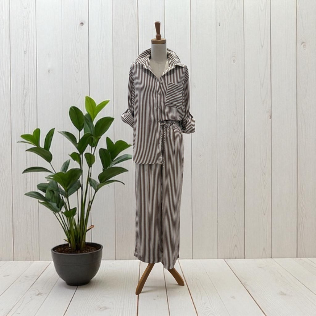 Mannequin wearing a striped outfit next to a potted plant against a light wooden panel background