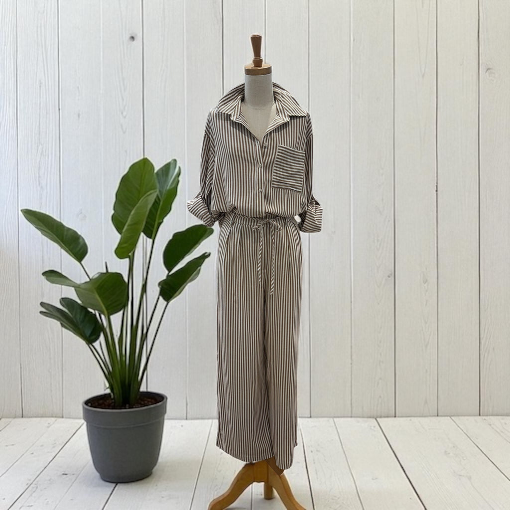 Striped shirt and pants set on a mannequin next to a potted plant against a white wooden panel background