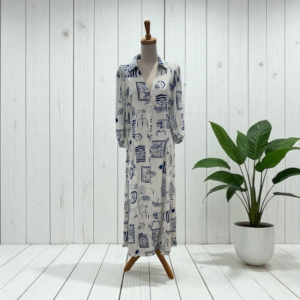 Long patterned dress on a mannequin with a plant in the background against a white wooden panel wall.