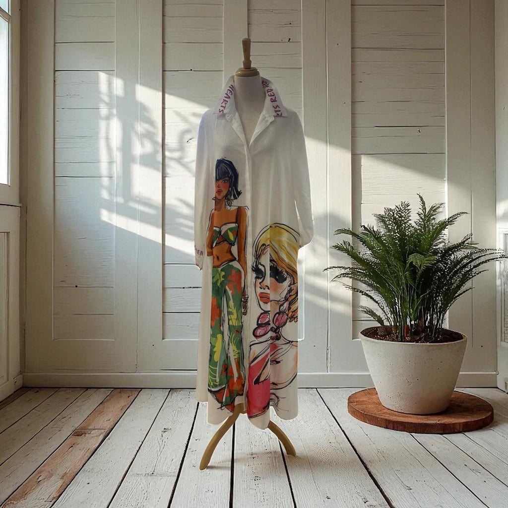 Mannequin wearing a white shirt with artistic designs in a room with a wooden floor and a plant.