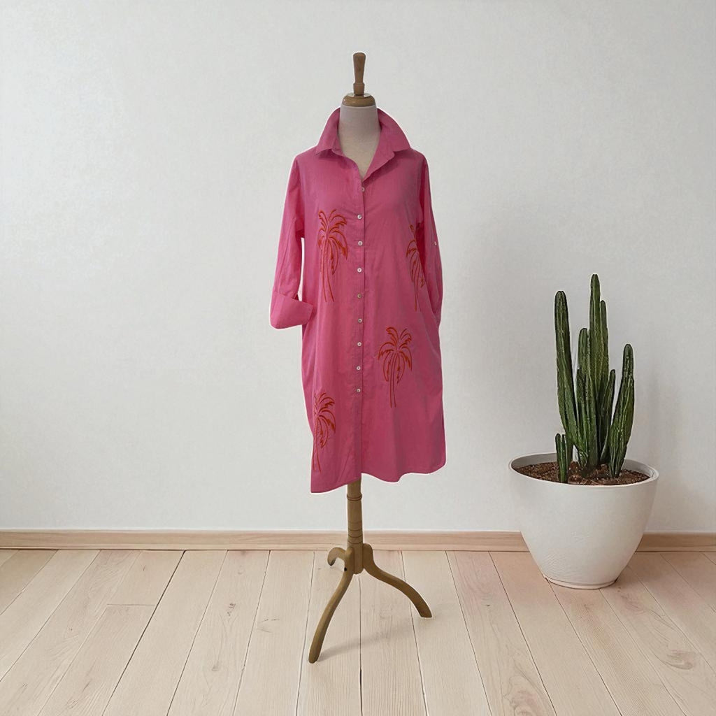 Pink dress on a mannequin with palm tree designs next to a potted cactus on a wooden floor.