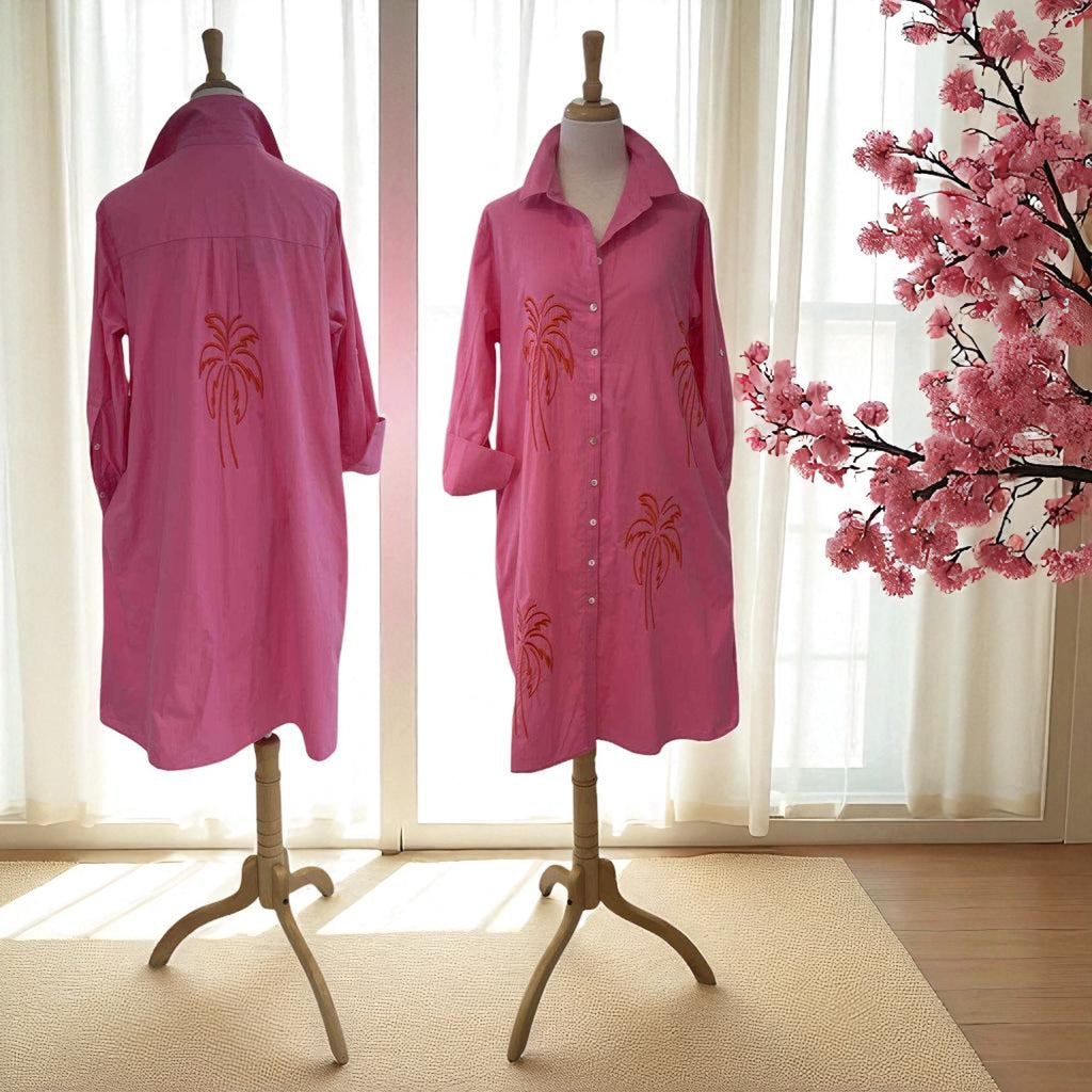 Two pink raincoats with palm tree designs on mannequins in a room with cherry blossoms.