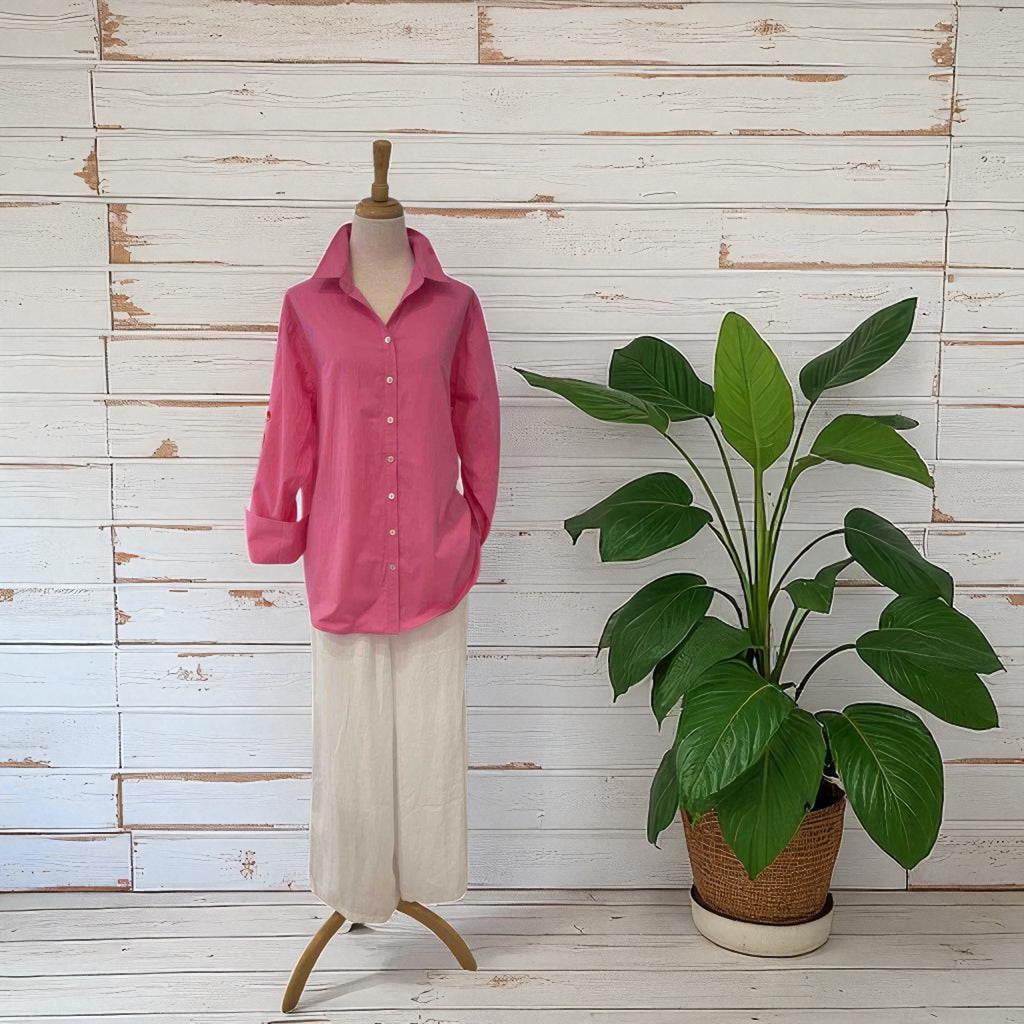 Mannequin wearing a pink shirt with a potted plant against a wooden wall.