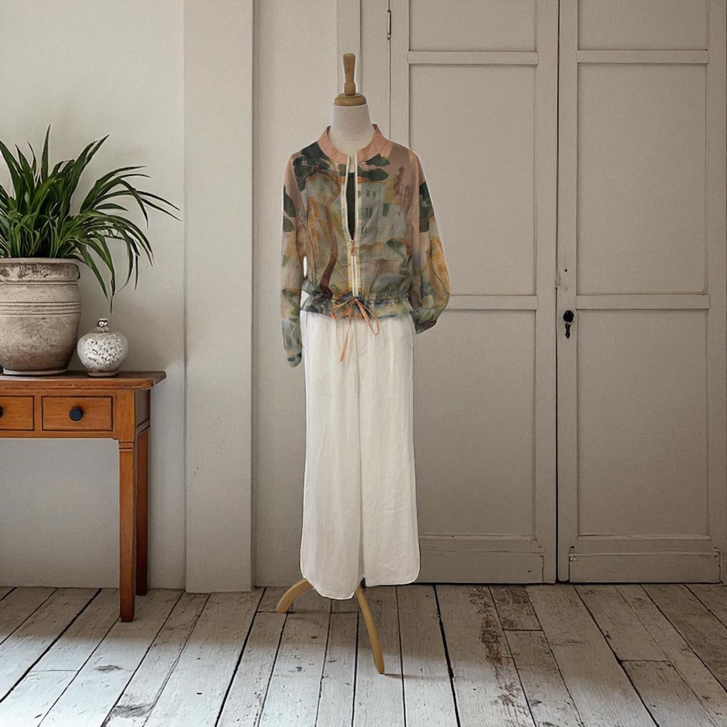 Mannequin wearing a floral blouse and white pants in a room with wooden floor and plant.