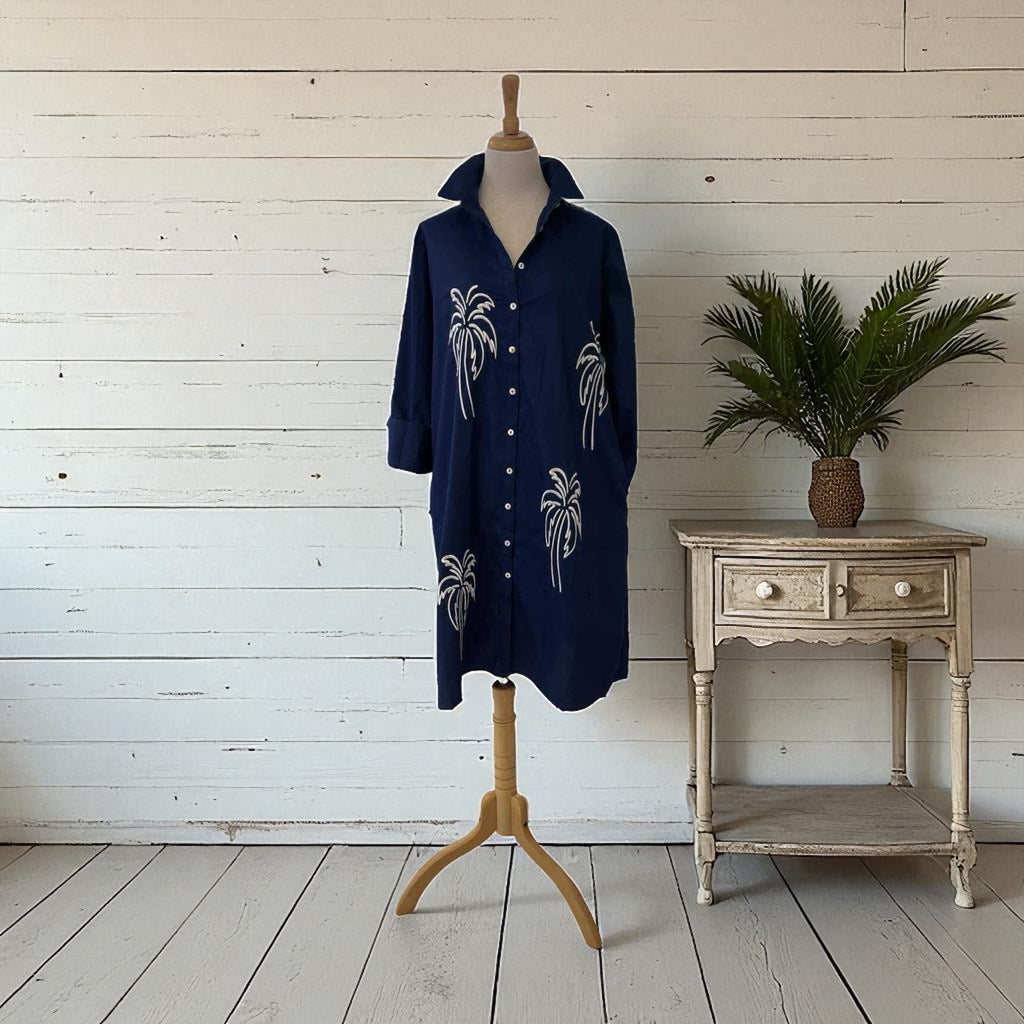 Navy blue shirt with white palm tree patterns on a mannequin against a wooden wall.