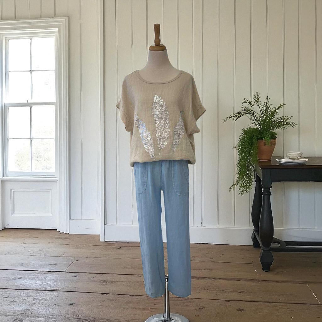 Mannequin wearing a beige sweater with sequin details and light blue pants in a room with wooden flooring and a window.