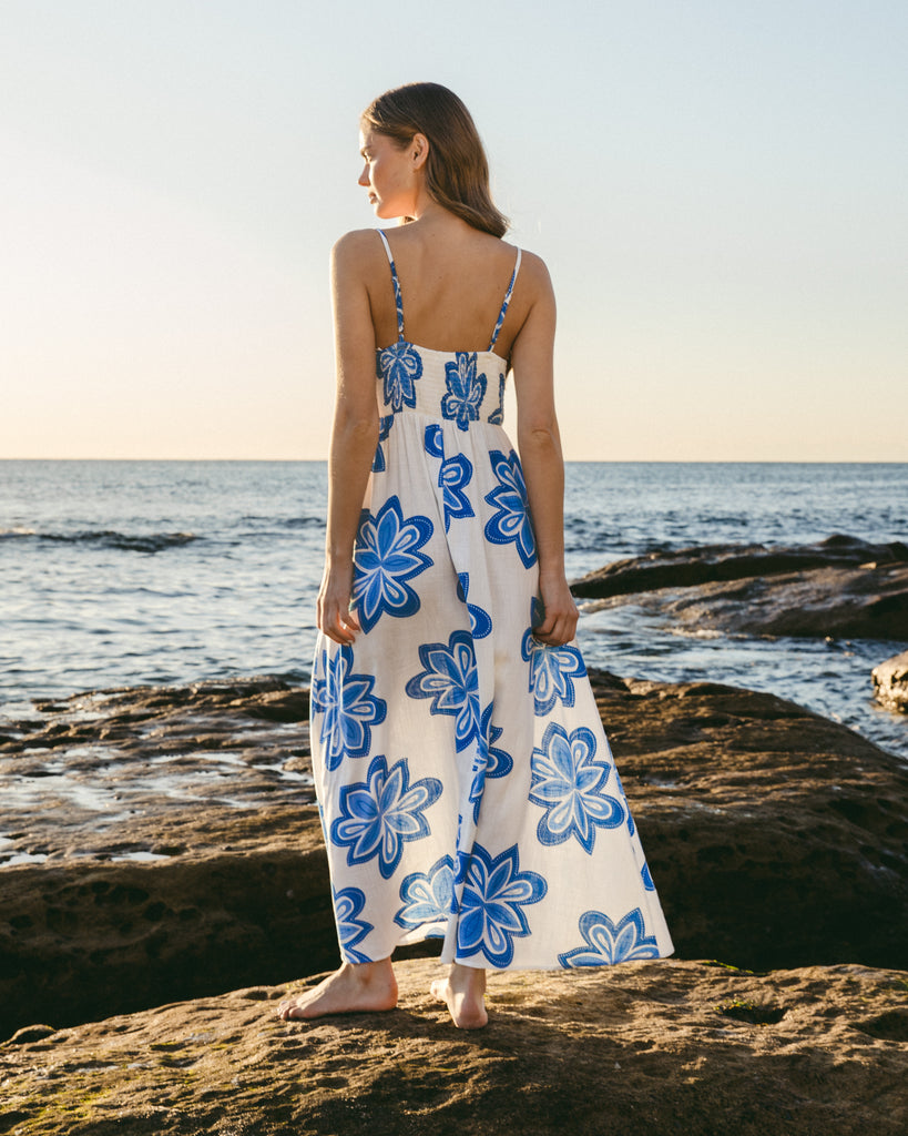 Woman in a floral dress standing on a rocky beach with ocean view