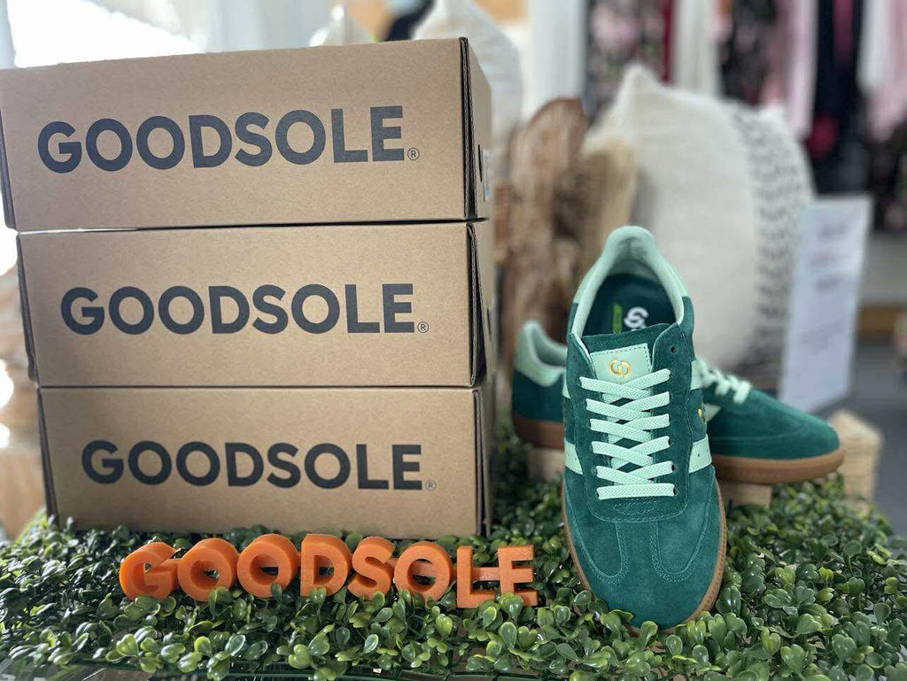 Green sneakers with white laces next to GOODSOLE boxes on a grass-like surface.